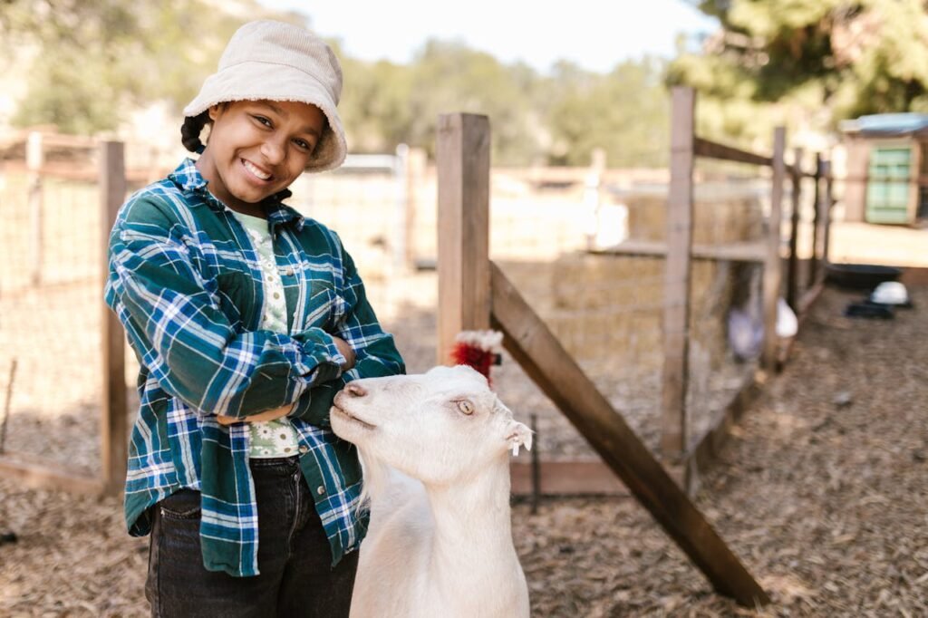 A cheerful girl poses with a goat on a sunny rural farm.